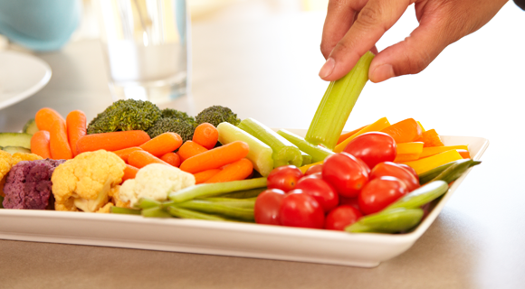 Hand taking celery from plate of raw vegetables