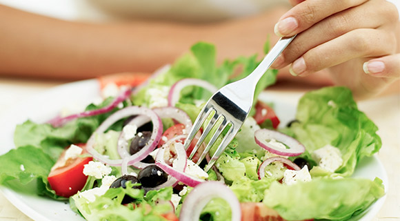 Woman sticking fork in a salad with vegetables
