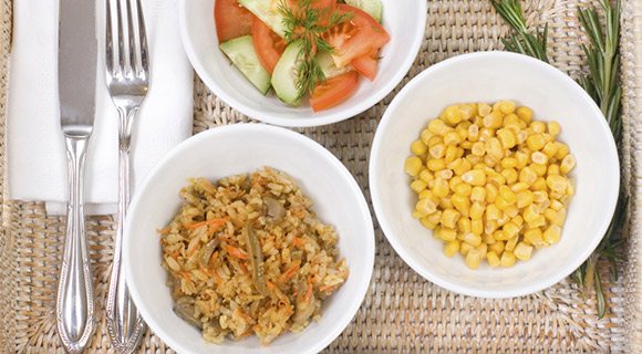 Three plates on a place mat with corn, vegetables and rice with a fork to the side