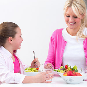 Woman pouring daughter water from a pitcher as they eat a salad