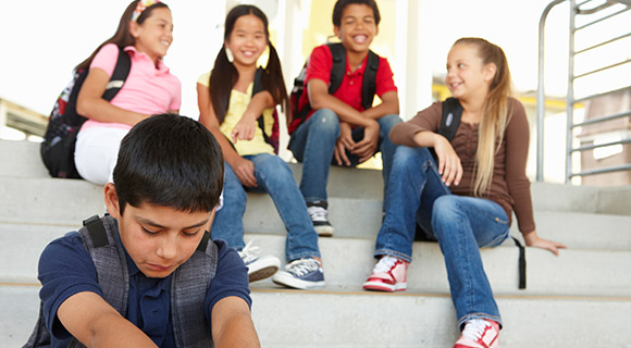 Group of kids sitting on stairs laughing and sad boy sitting alone to the side
