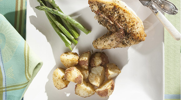 White plate with grilled chicken breast, asparagus, and sliced potatoes
