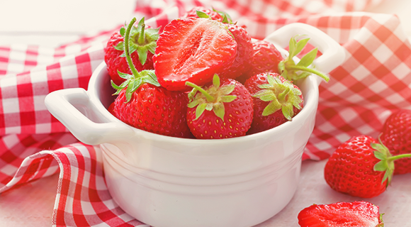 Fresh strawberries in a white bowl on a red checked napkin