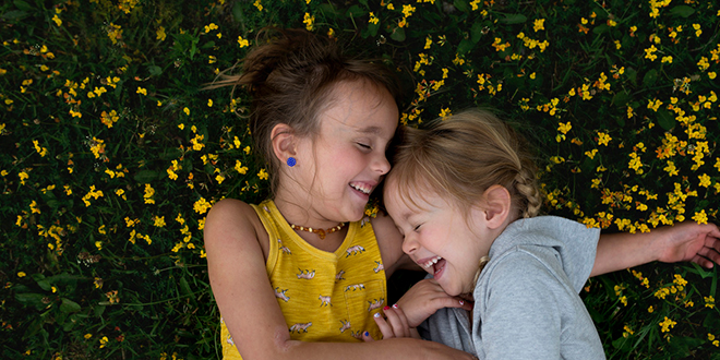Dos chicas jóvenes riendo mientras está acostado en la flor cubierta de hierba.
