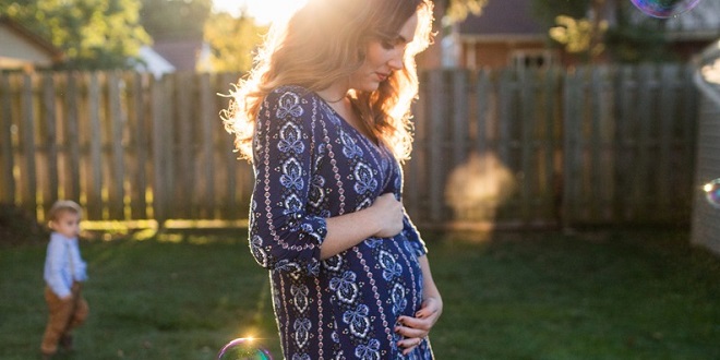 Una mujer embarazada está de pie en el césped tomando el sol.