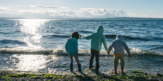3 niños de pie en aguas poco profundas a lo largo de la costa del océano.